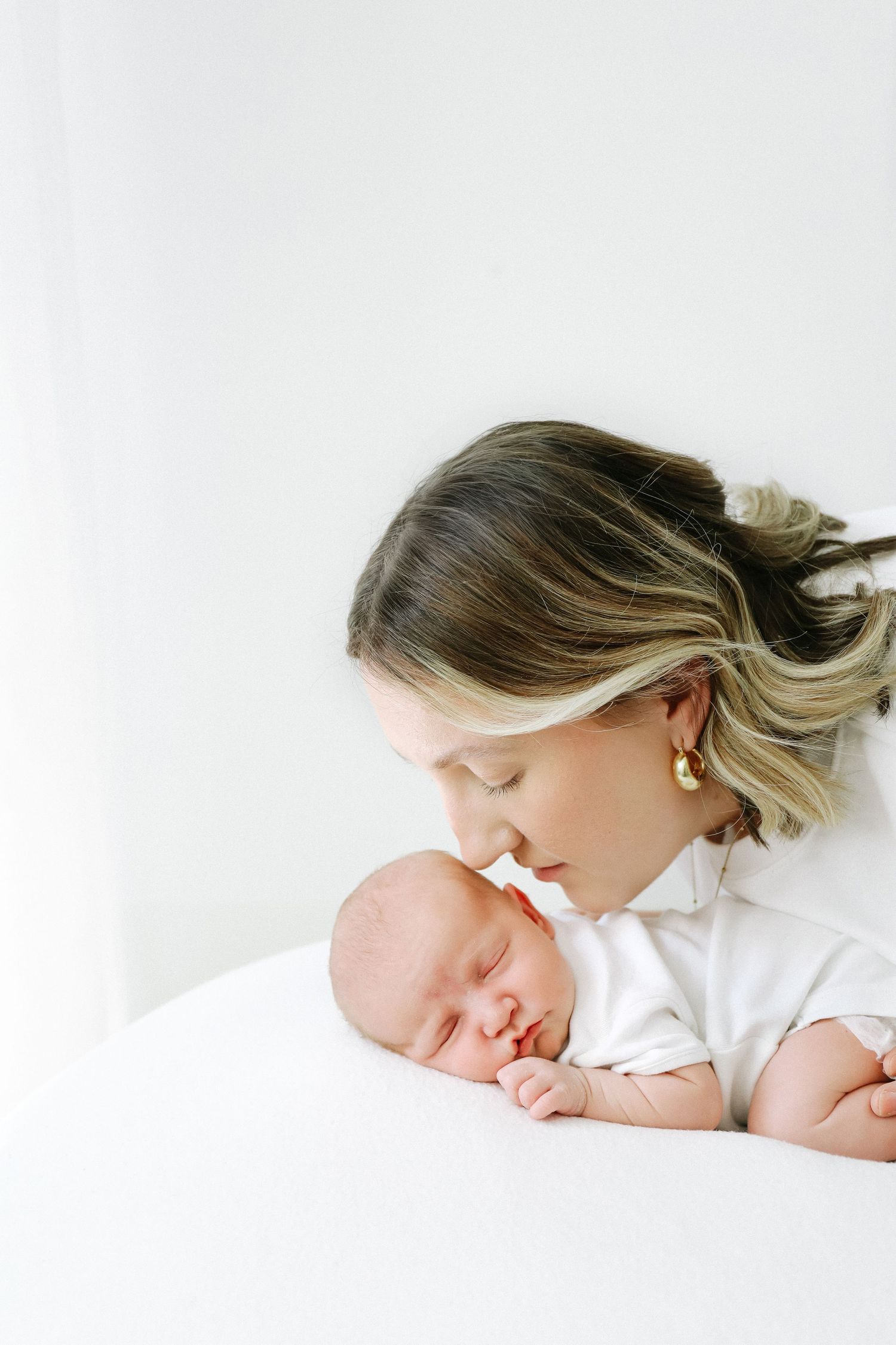 Tender moment showing parent in white snuggling with sleeping newborn baby against light background during newborn shoot in Nottingham