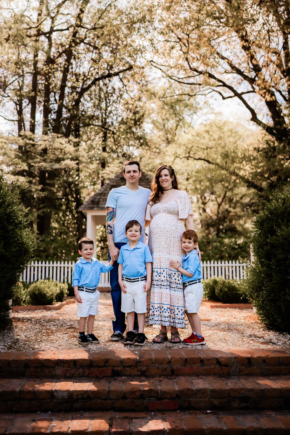 Family in coordinating blue and white outfits poses together on a brick wall with autumn trees.