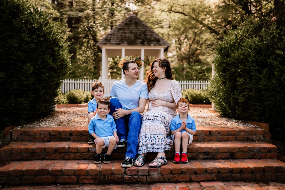 Family sitting on brick steps surrounded by lush trees and autumn foliage creates warm outdoor portrait scene.