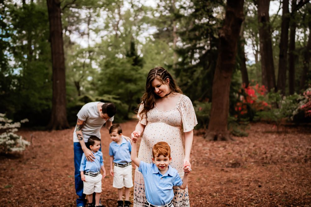 Family enjoying outdoor portrait session among fall foliage and pine trees.