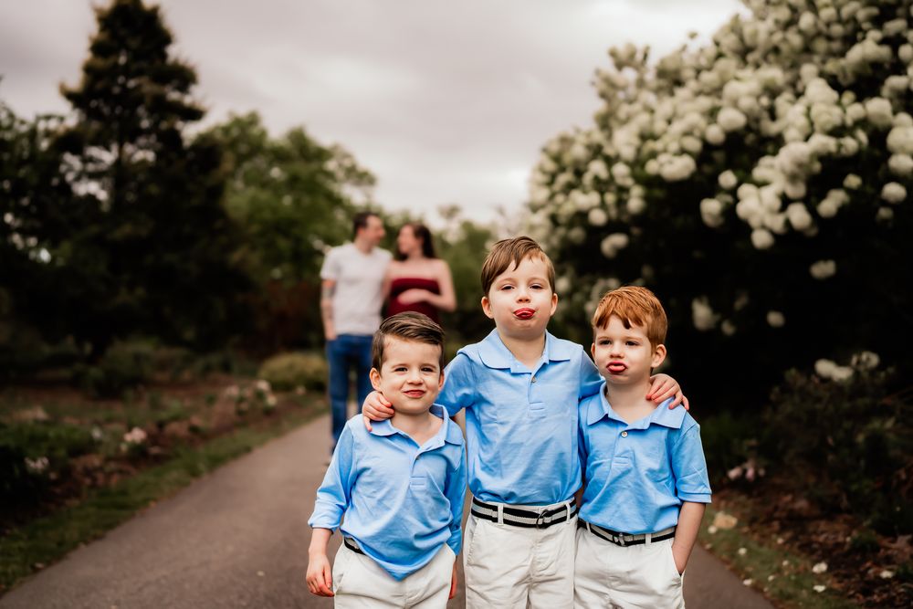 A family wearing blue and white outfits walks down a tree-lined pathway with blooming white flowers.