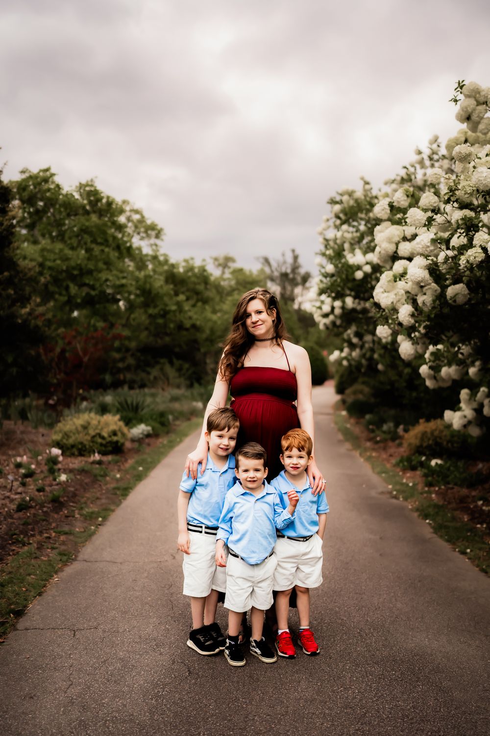 A family poses on a dirt path lined with blooming white hydrangea bushes on an overcast day.