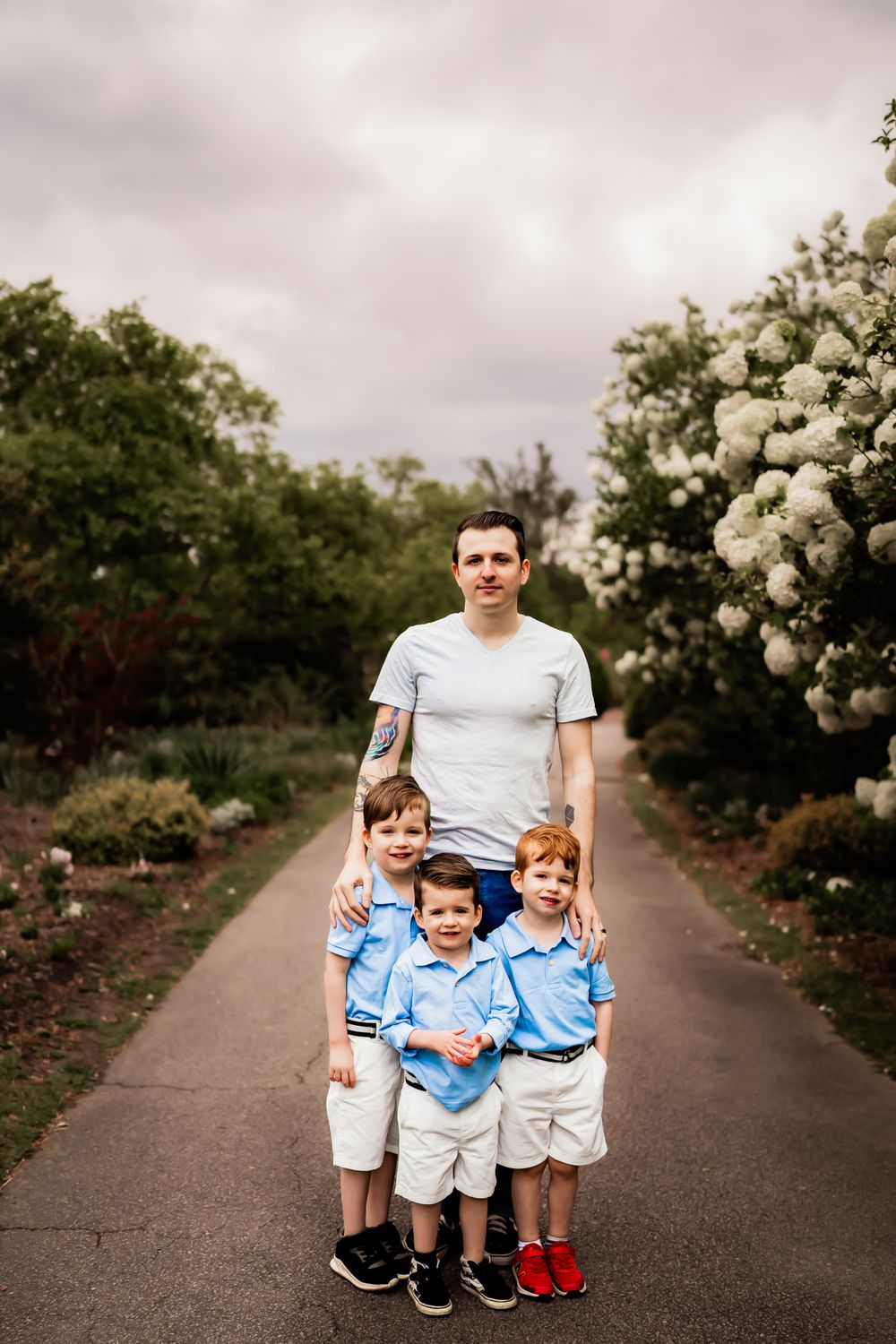 A group poses together on a path surrounded by flowering white hydrangea bushes under an overcast sky.