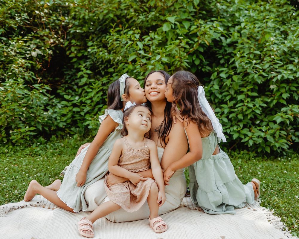 A candid group moment of affection and laughter while sitting together on a blanket in a lush garden setting.