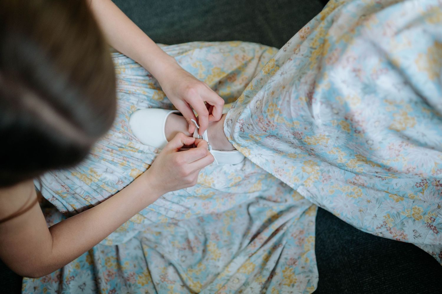 Two hands gently touch while resting on a light blue floral patterned fabric.