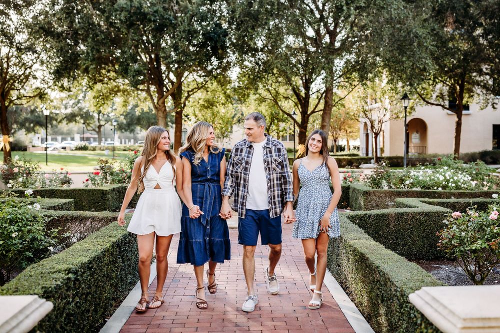 People walking together outdoors in casual summer clothing along tree-lined pathways on a sunny day.