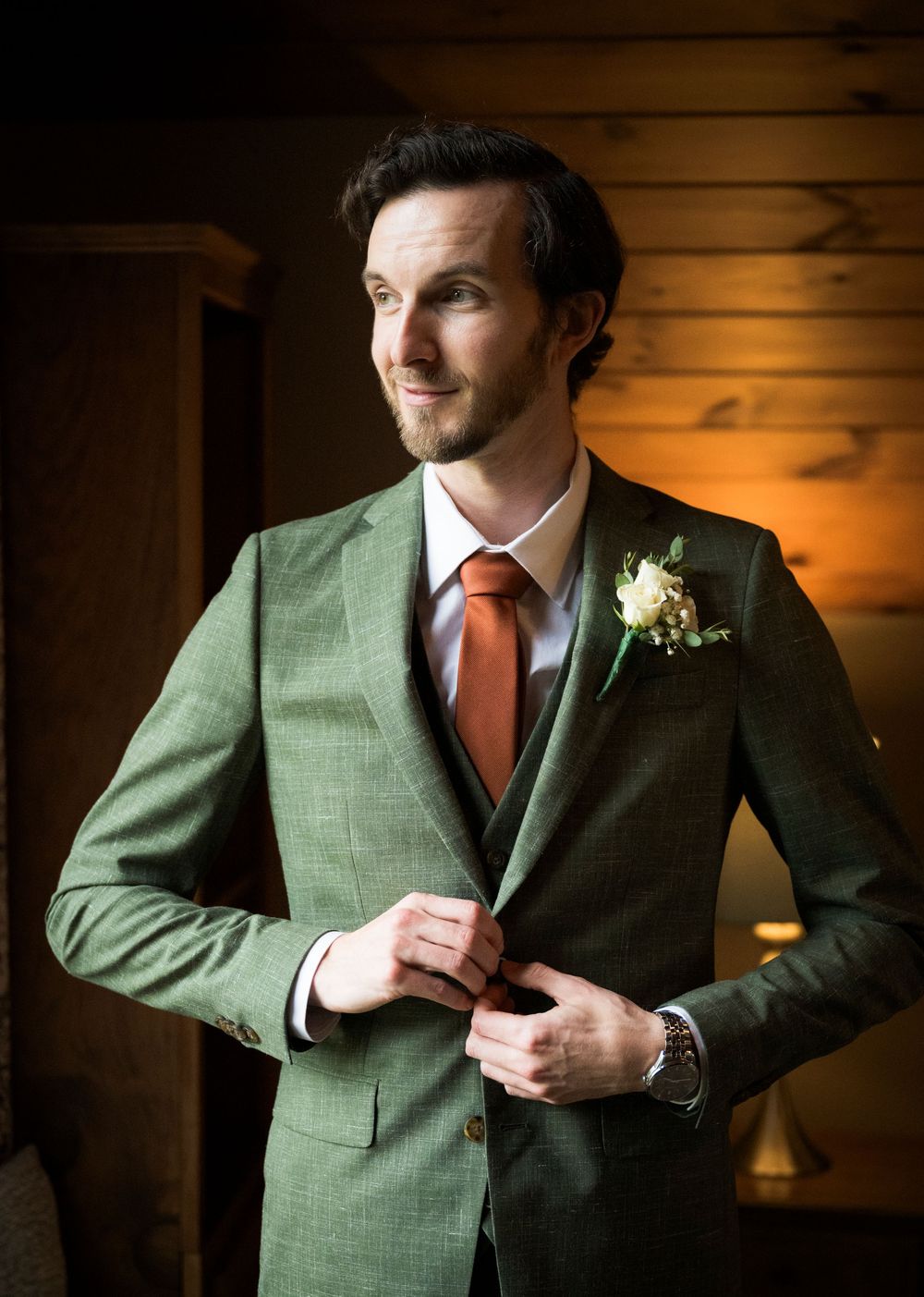 Close-up sequence of a green suit jacket with orange tie and boutonniere being adjusted in warm lighting.