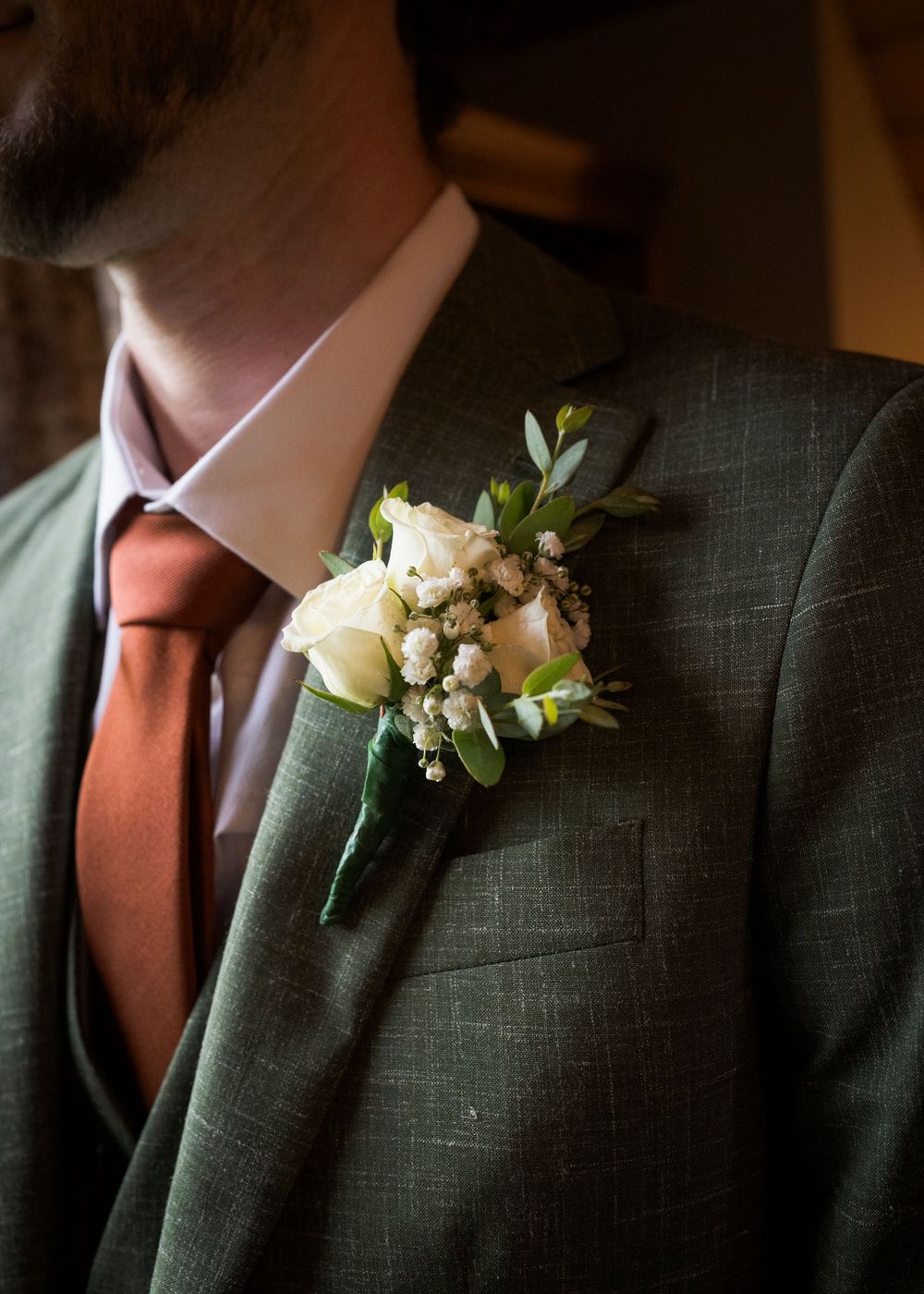 Close-up details of a formal green suit jacket with a rust-colored tie and white floral boutonniere.