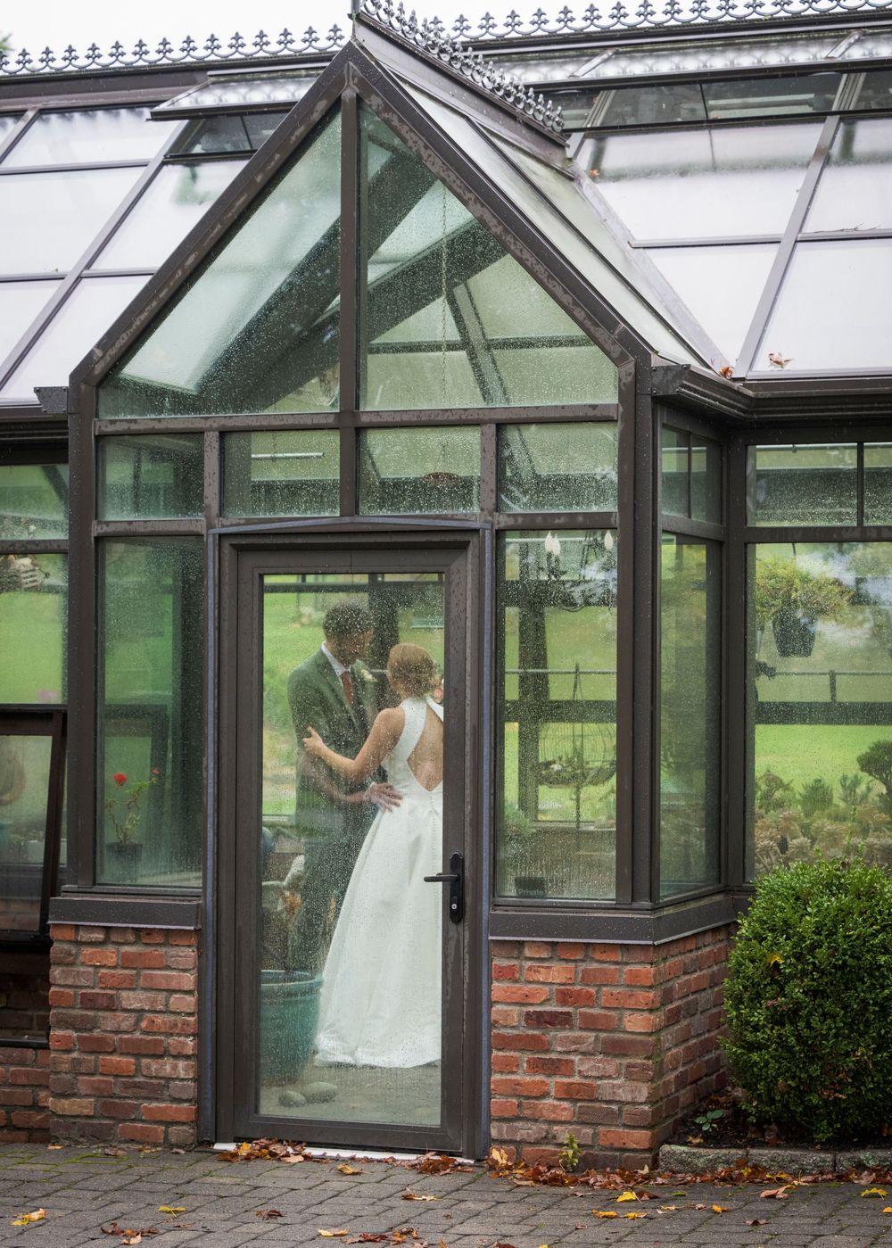 A series of photos showing a greenhouse with brick base and glass panels in a garden setting.
