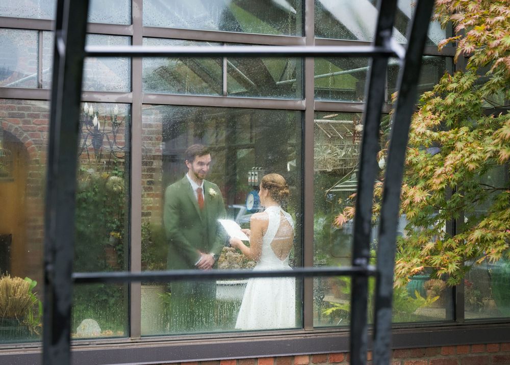 Wedding couple shares intimate moment in modern glass conservatory surrounded by natural light and greenery.