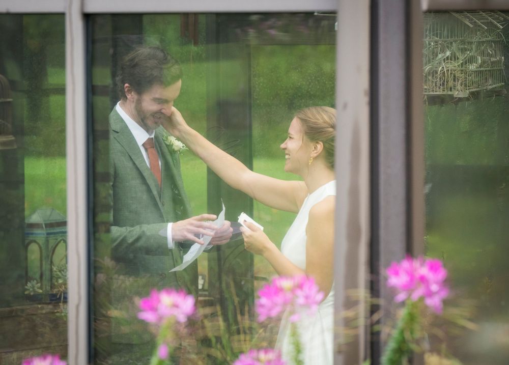 Couple exchanges vows in elegant greenhouse setting with pink flowers in foreground.
