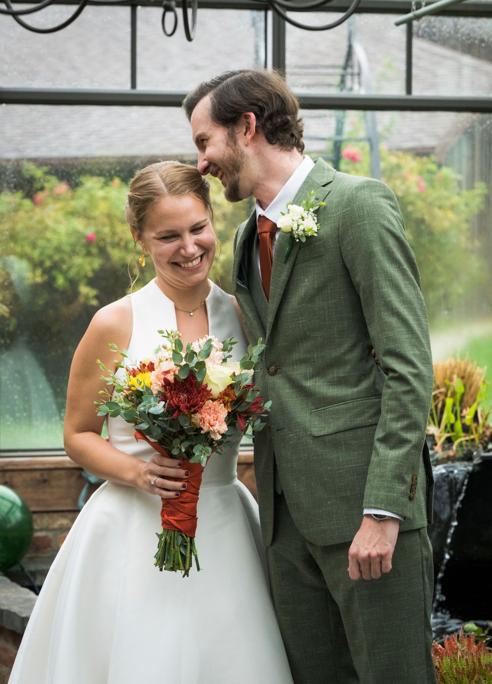 A wedding couple shares joyful moments in a greenhouse setting with vibrant autumn florals.