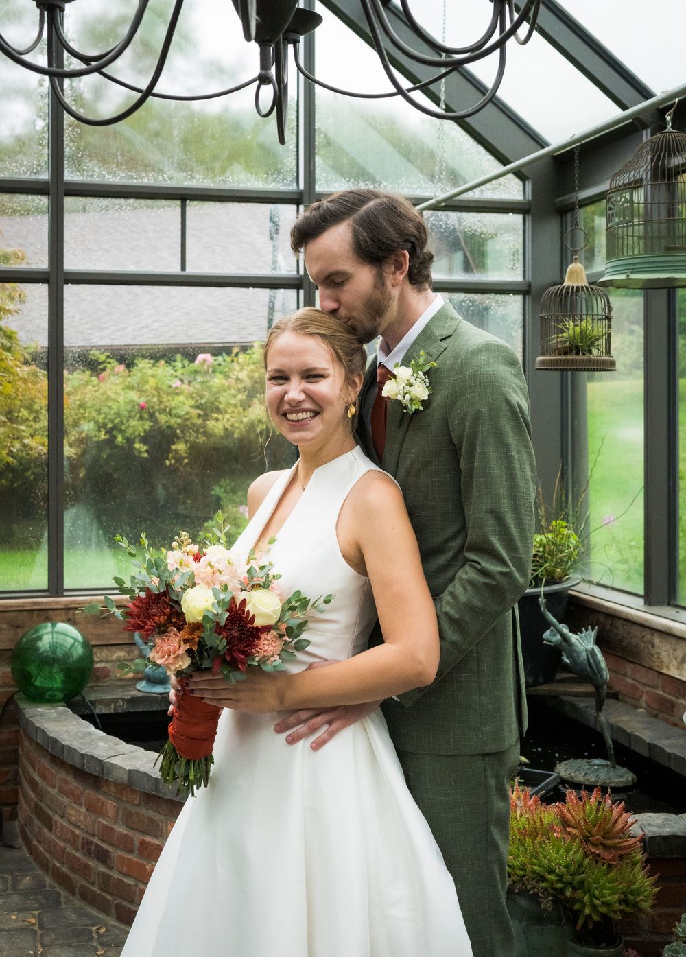 Wedding couple poses together inside a rustic greenhouse filled with plants and natural light.