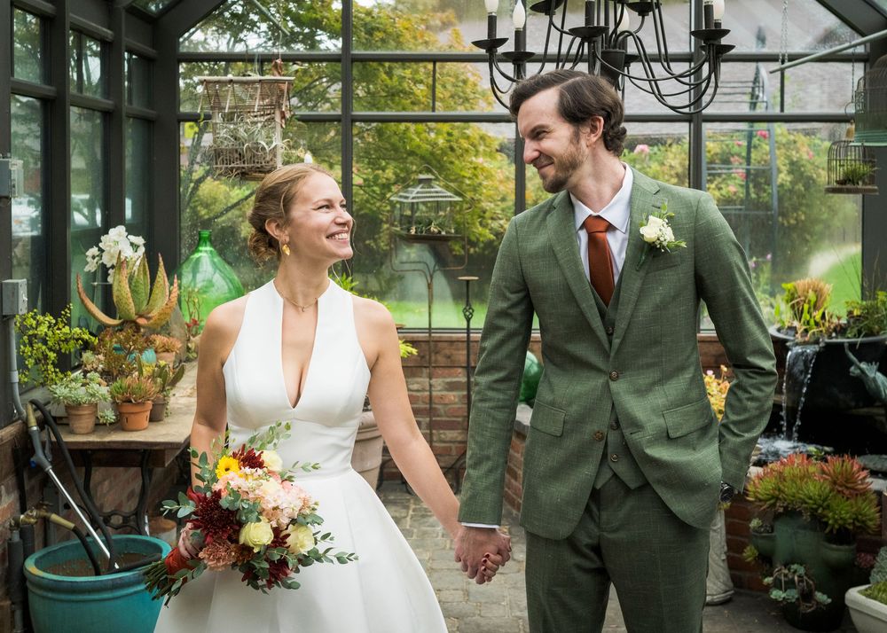 Newlyweds share a joyful moment in a greenhouse filled with natural light and greenery.