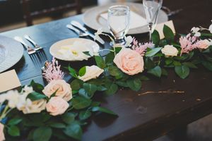 Table settings with pastel pink roses and greenery floral arrangements at an elegant wedding reception event.