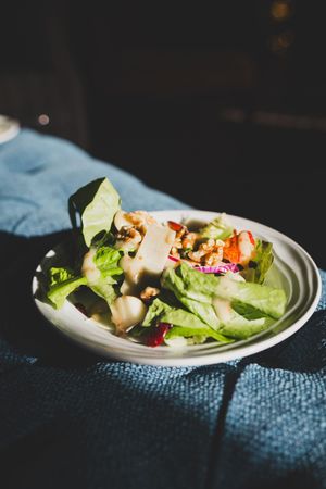 Fresh garden salad served on a white plate featuring crisp lettuce, vegetables and dressing in dramatic lighting.