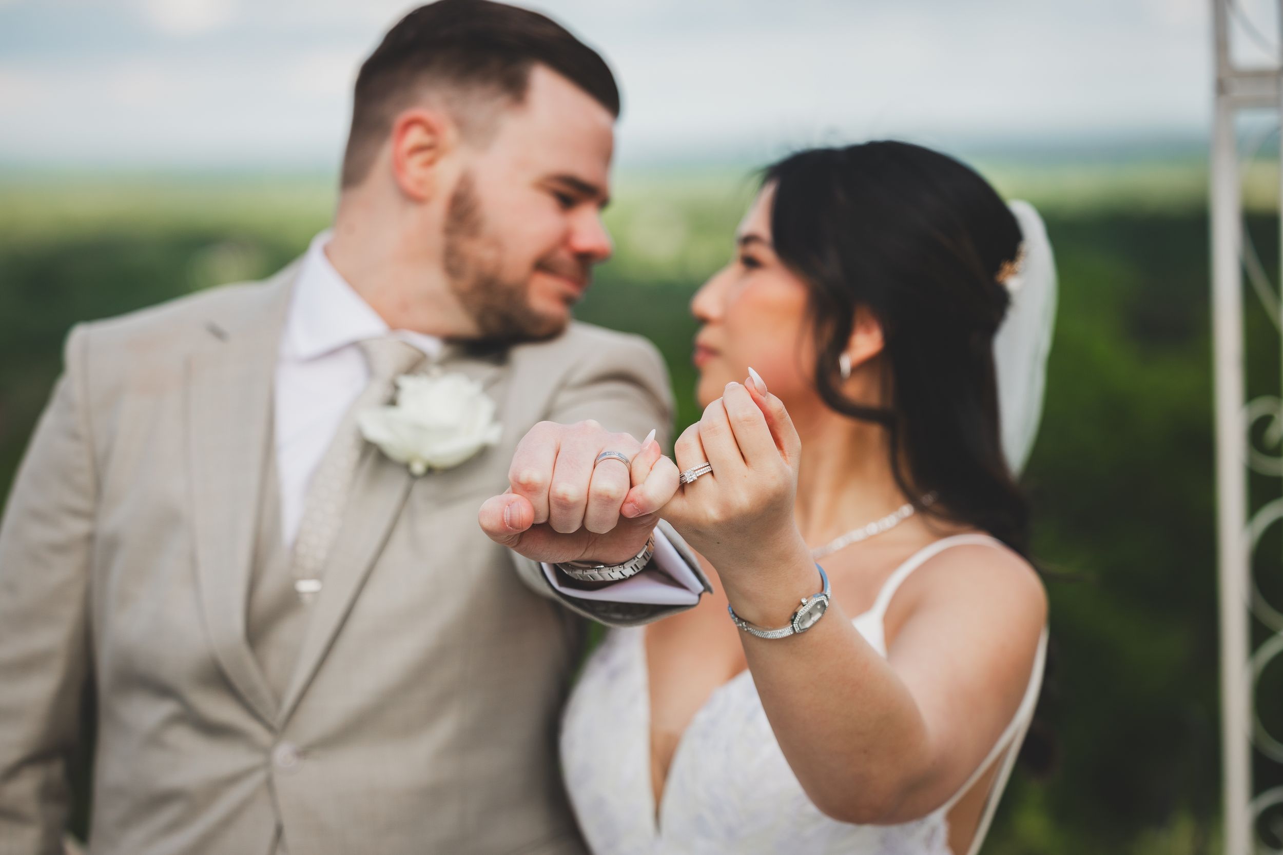 A couple in wedding attire share an intimate moment together outdoors with the groom in beige and bride in white.