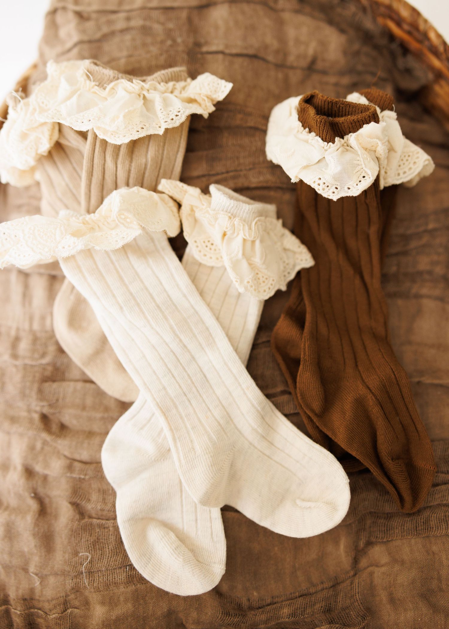 Vintage knitted baby bonnet with lace trim and ties rests on delicate crocheted doily background in neutral beige tones.