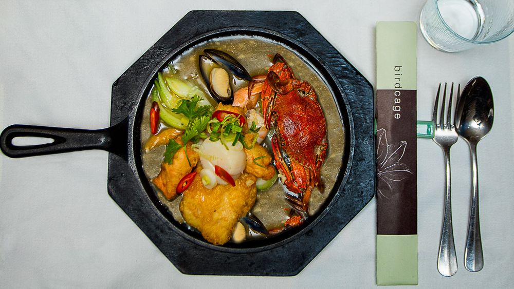 Seafood hot pot with crab and fish served in a black cast iron skillet with utensils.