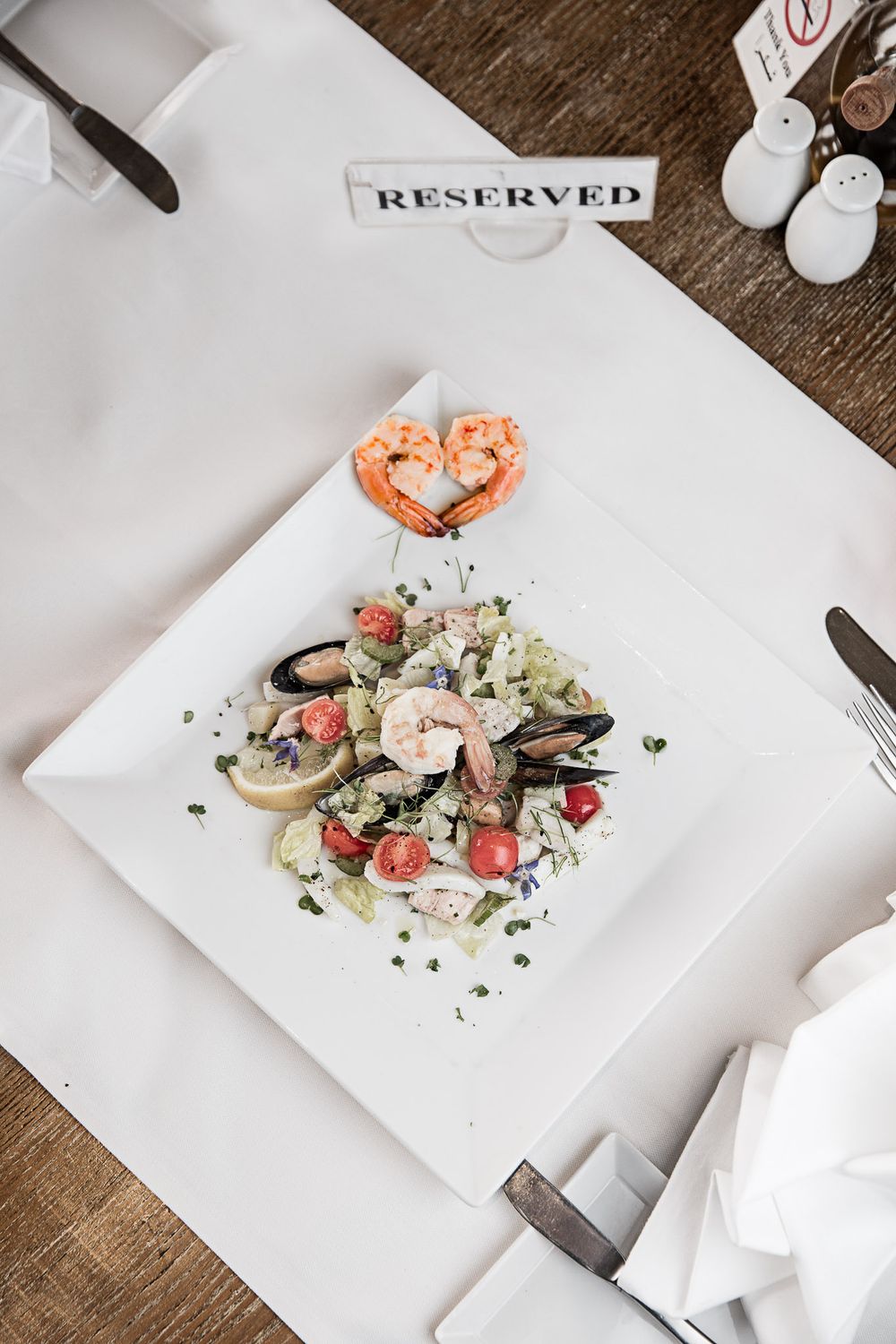 Elegant seafood salad with shrimp and fresh garnishes on a white plate marked 'Reserved'.