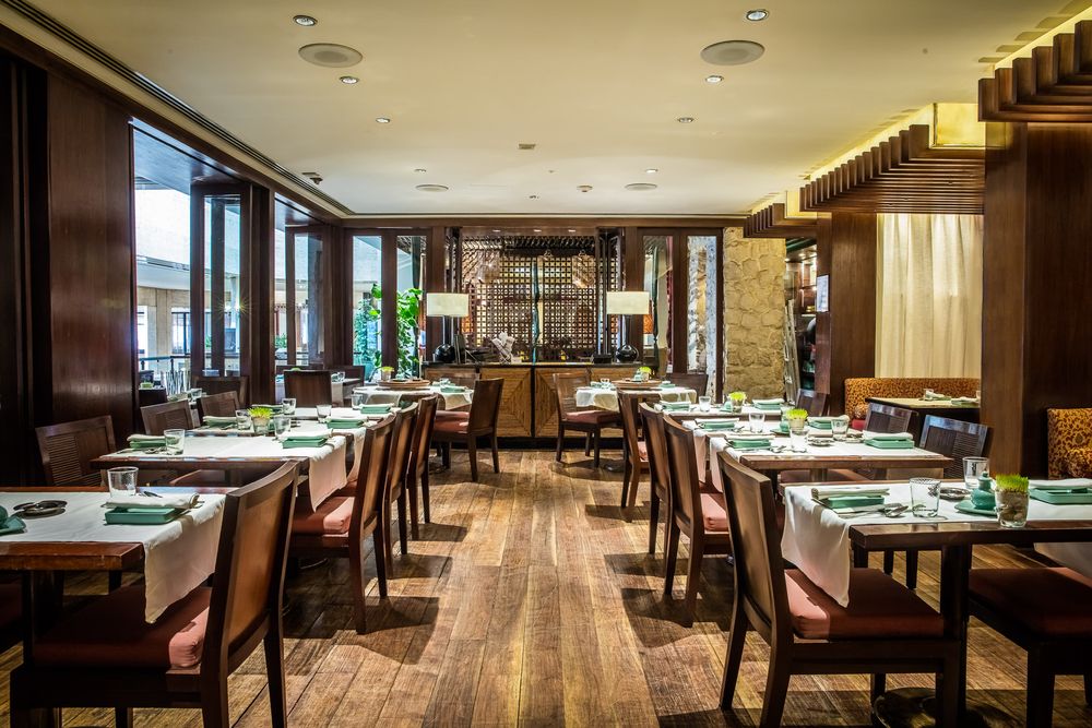 Modern restaurant interior with wooden floors and tables set for dining service.