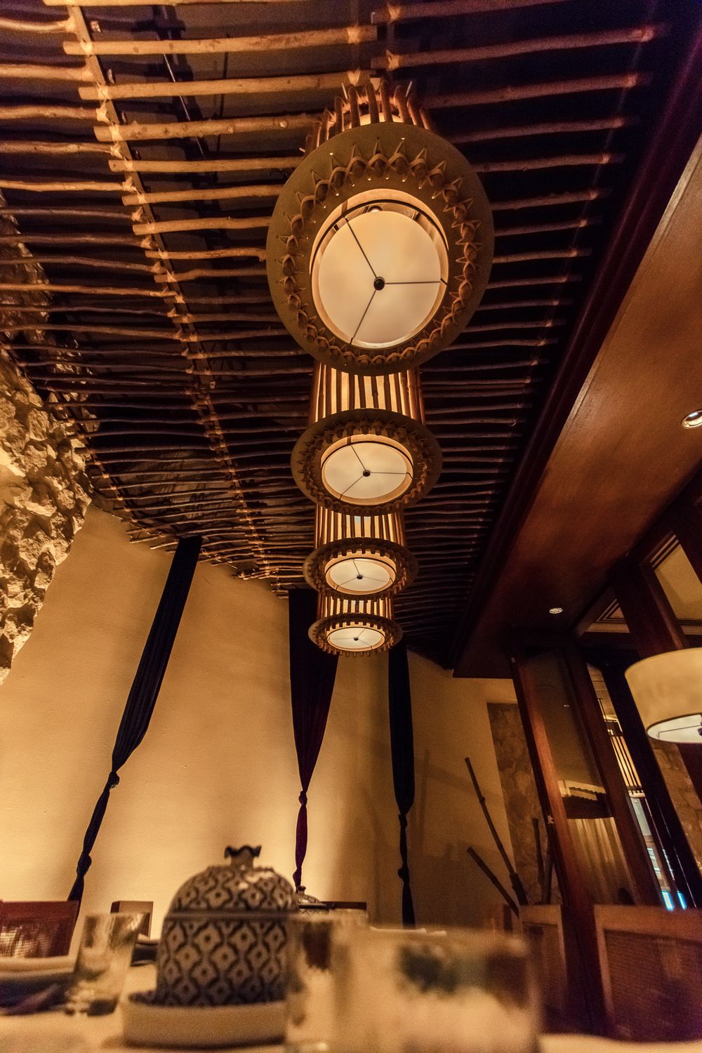Elegant restaurant interior with ornate pendant lights and exposed wooden beams creating warm ambiance.