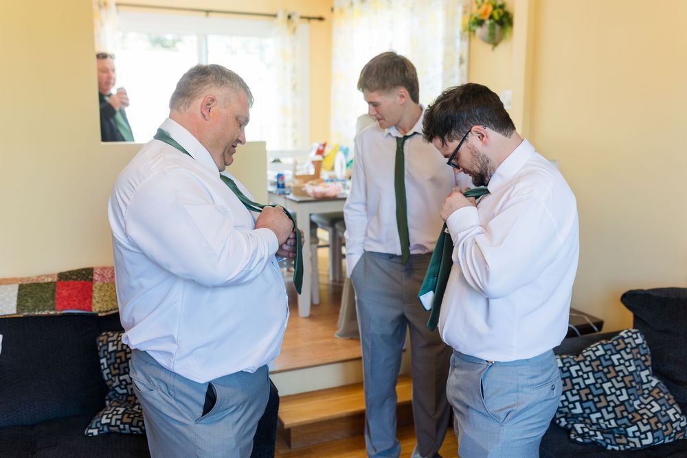 Three people in formal attire helping each other get dressed in a living room setting.