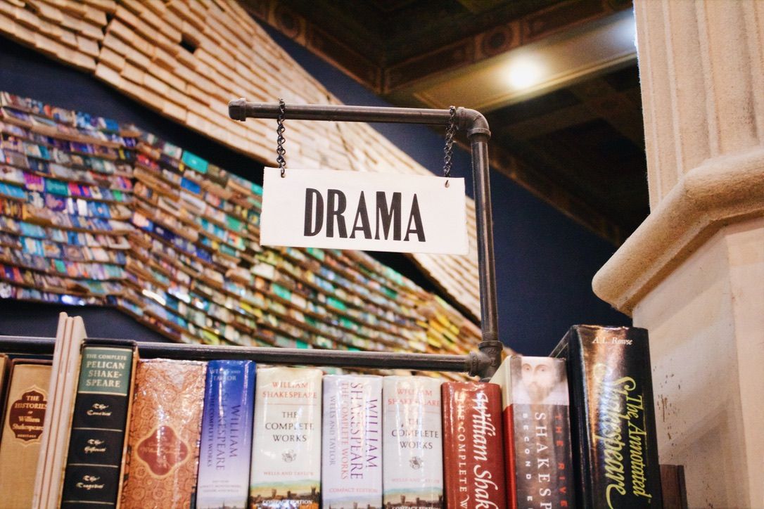 Library shelf with a DRAMA section sign and various book spines visible.