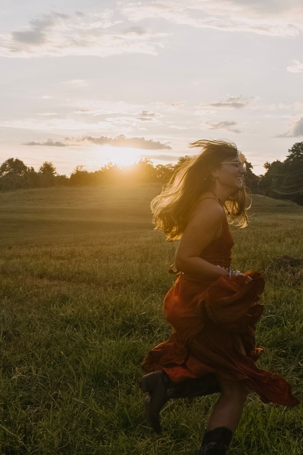 A silhouette dances in a flowing dress across a golden field at sunset as wind sweeps through their hair.