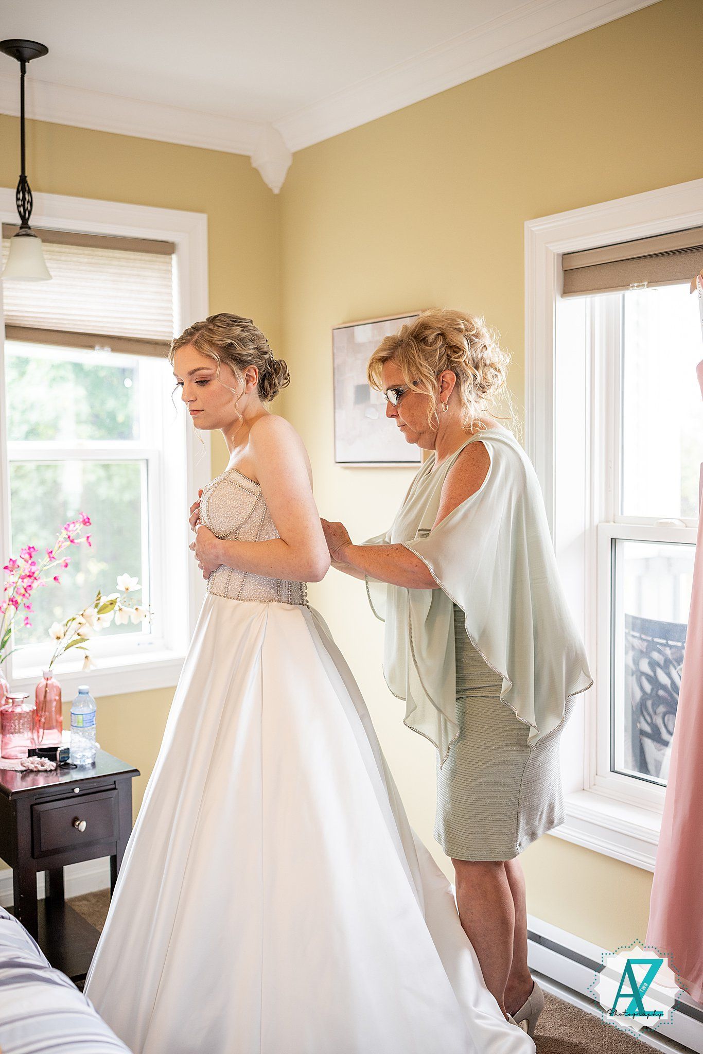 Wedding party helps bride get dressed in sun-filled room during preparation for the ceremony.