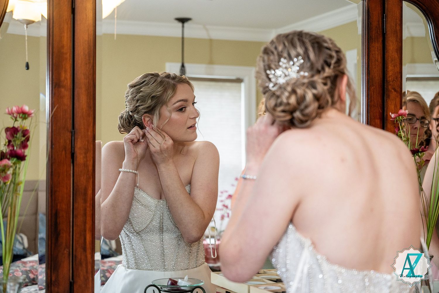 Wedding party members help with final touches of bridal preparation in elegant room with mirror.