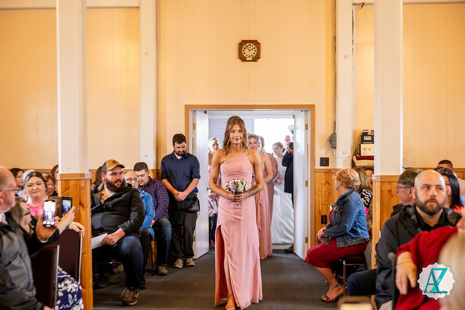 Wedding party members gather in a hallway with peach-colored walls and white columns.