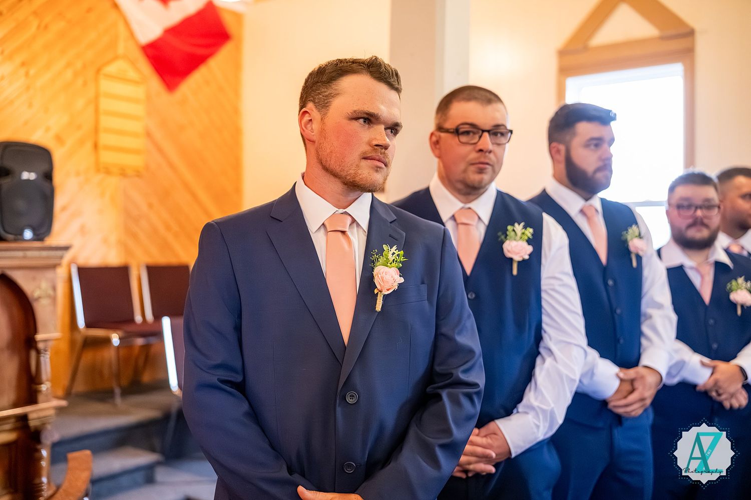 A row of formally dressed guests wearing blue suits stands lined up at a wedding reception event.