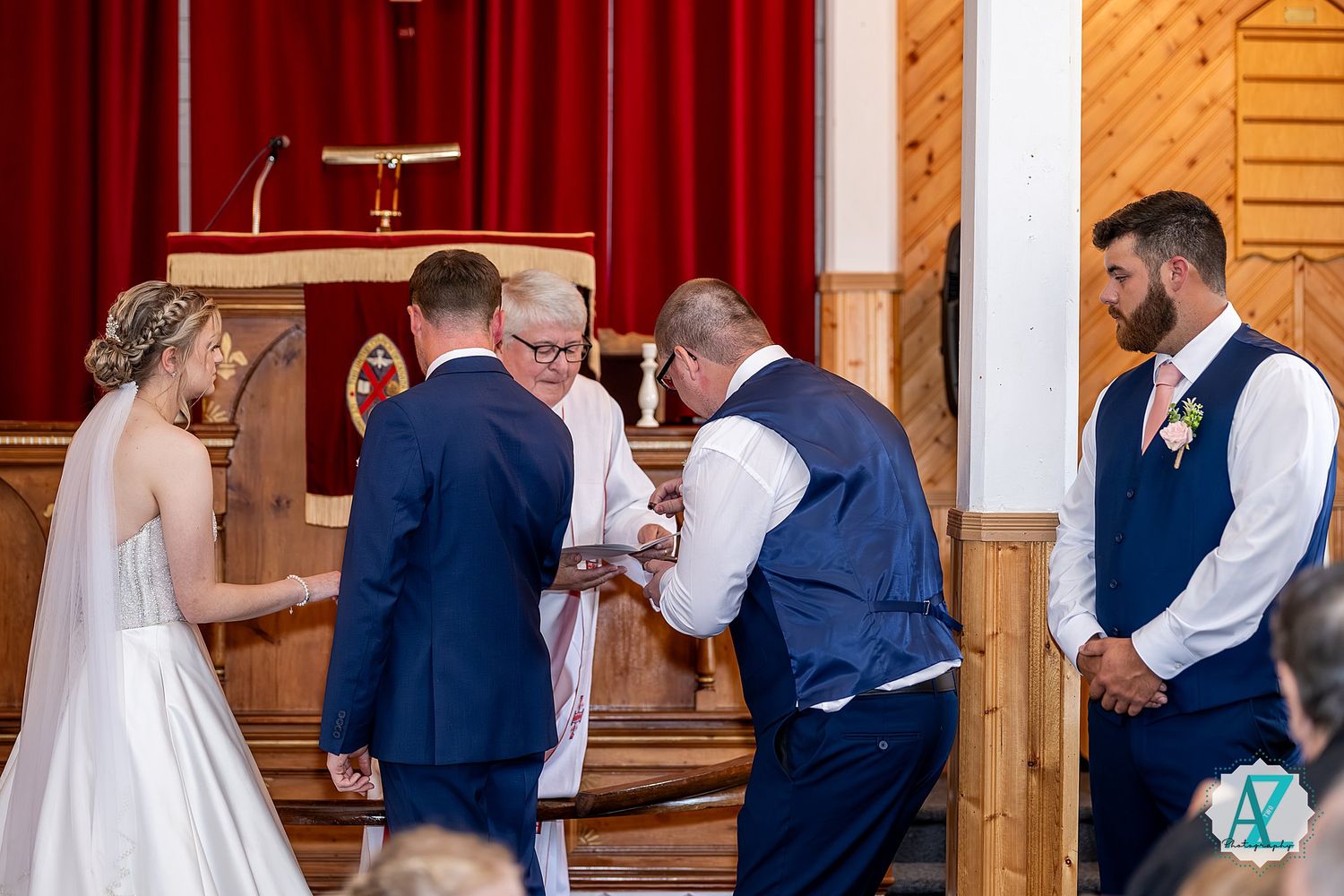 Wedding party members line up against a rustic wooden wall with red curtains during an indoor ceremony celebration.