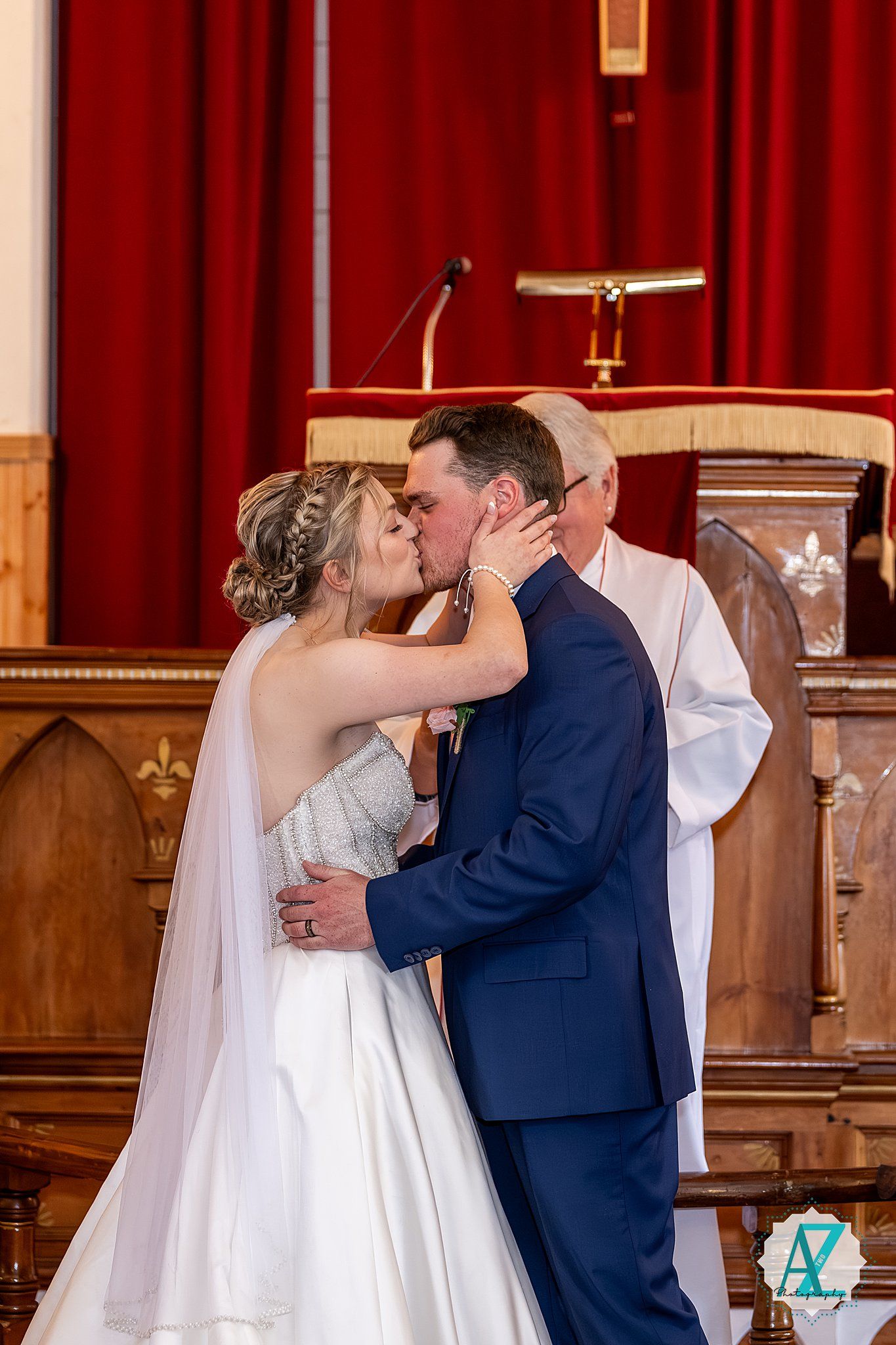 Wedding ceremony taking place in church sanctuary with red curtains.