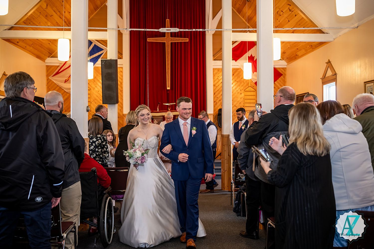Panoramic view of wedding guests mingling inside a church reception hall with wooden beams and crosses.