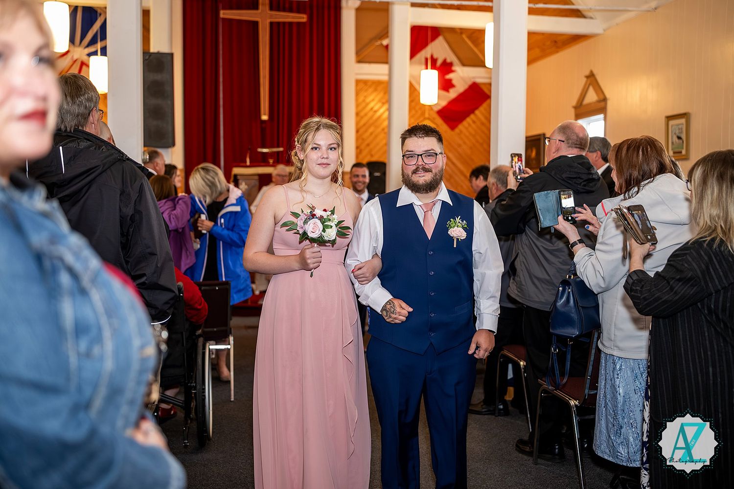 Wedding guests dancing and socializing at a reception in a church hall with wooden cross on the wall.