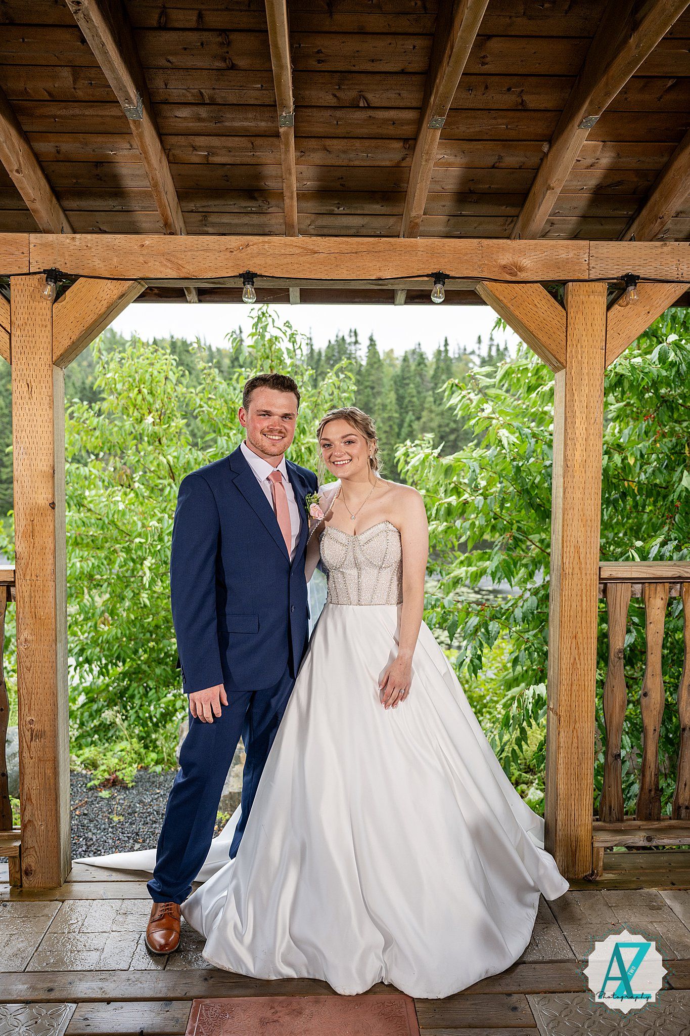 A covered wooden pavilion decorated for a wedding with green foliage visible in the background.