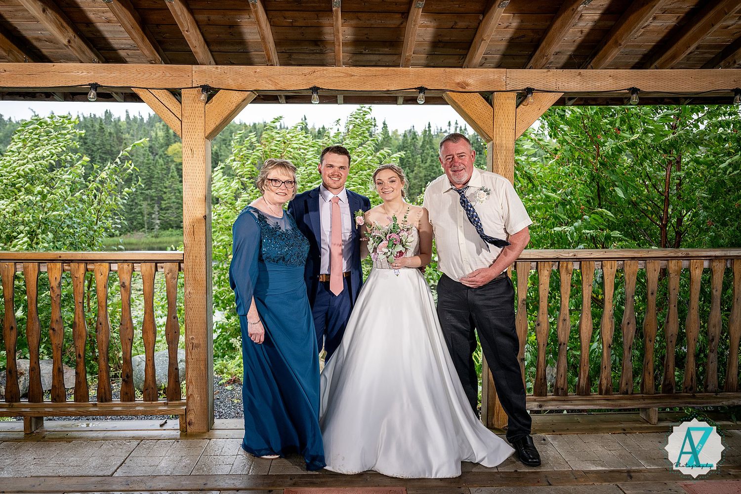 Wedding party poses under wooden beams on outdoor deck with forest backdrop.