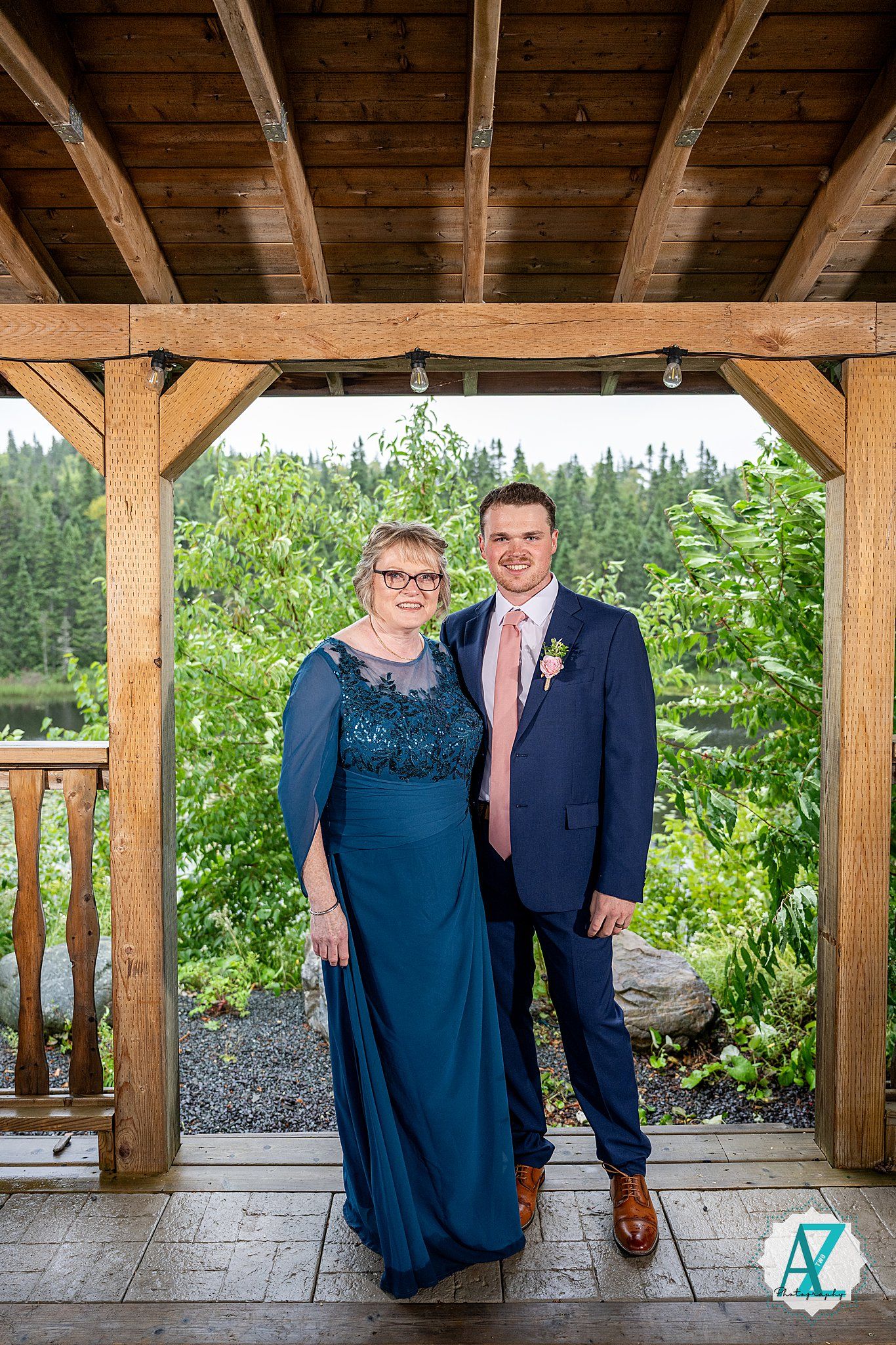 Wedding guests pose together under a rustic wooden pavilion surrounded by lush greenery.