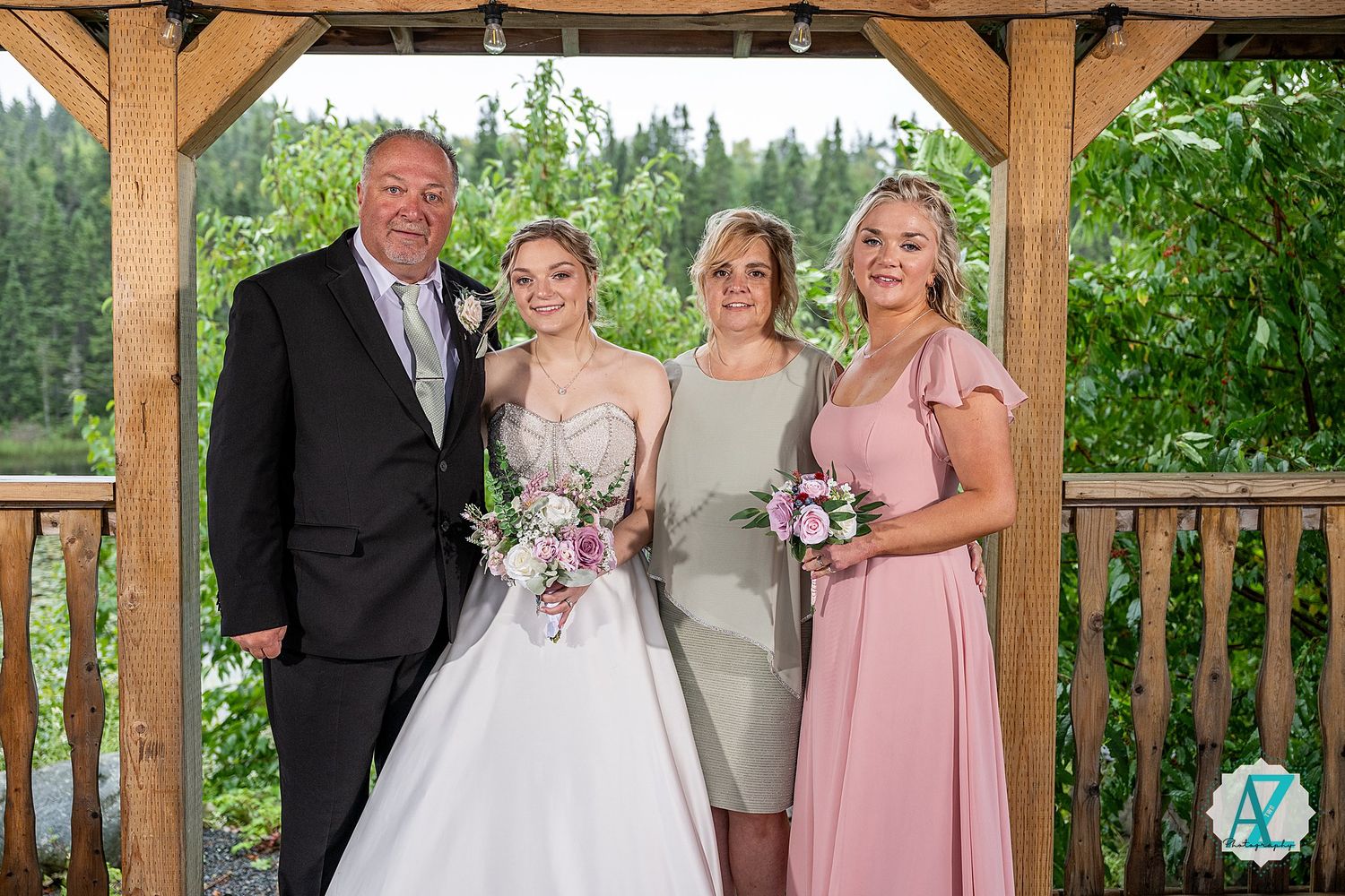 Formal group photo on rustic covered porch with pink bridesmaids dresses and forest scenery.
