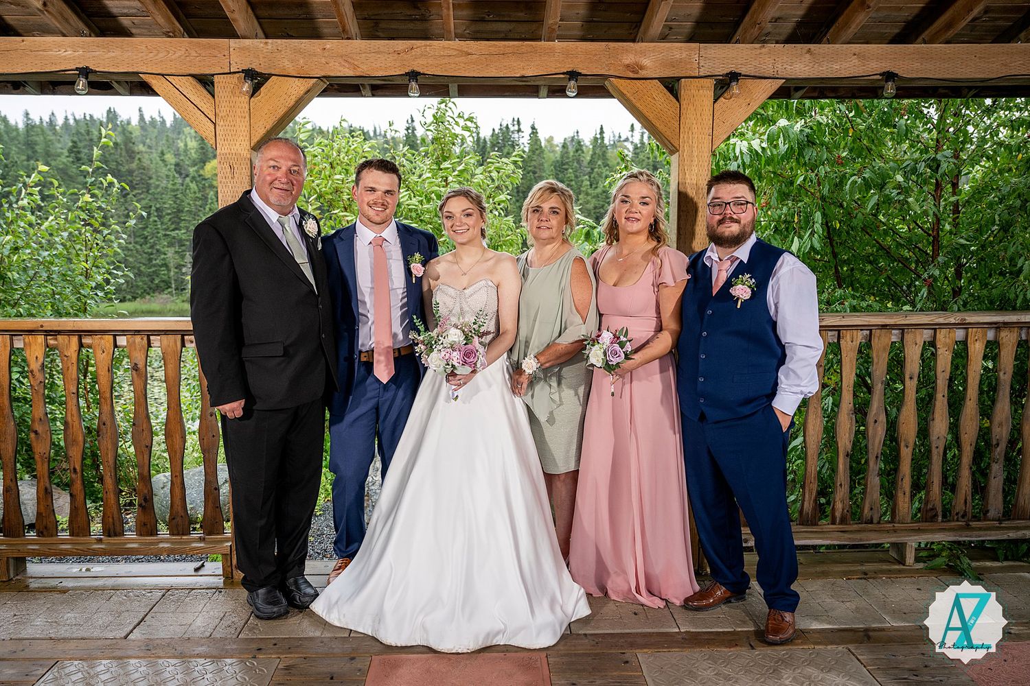 Wedding party gathers on covered wooden deck with natural woodland backdrop.