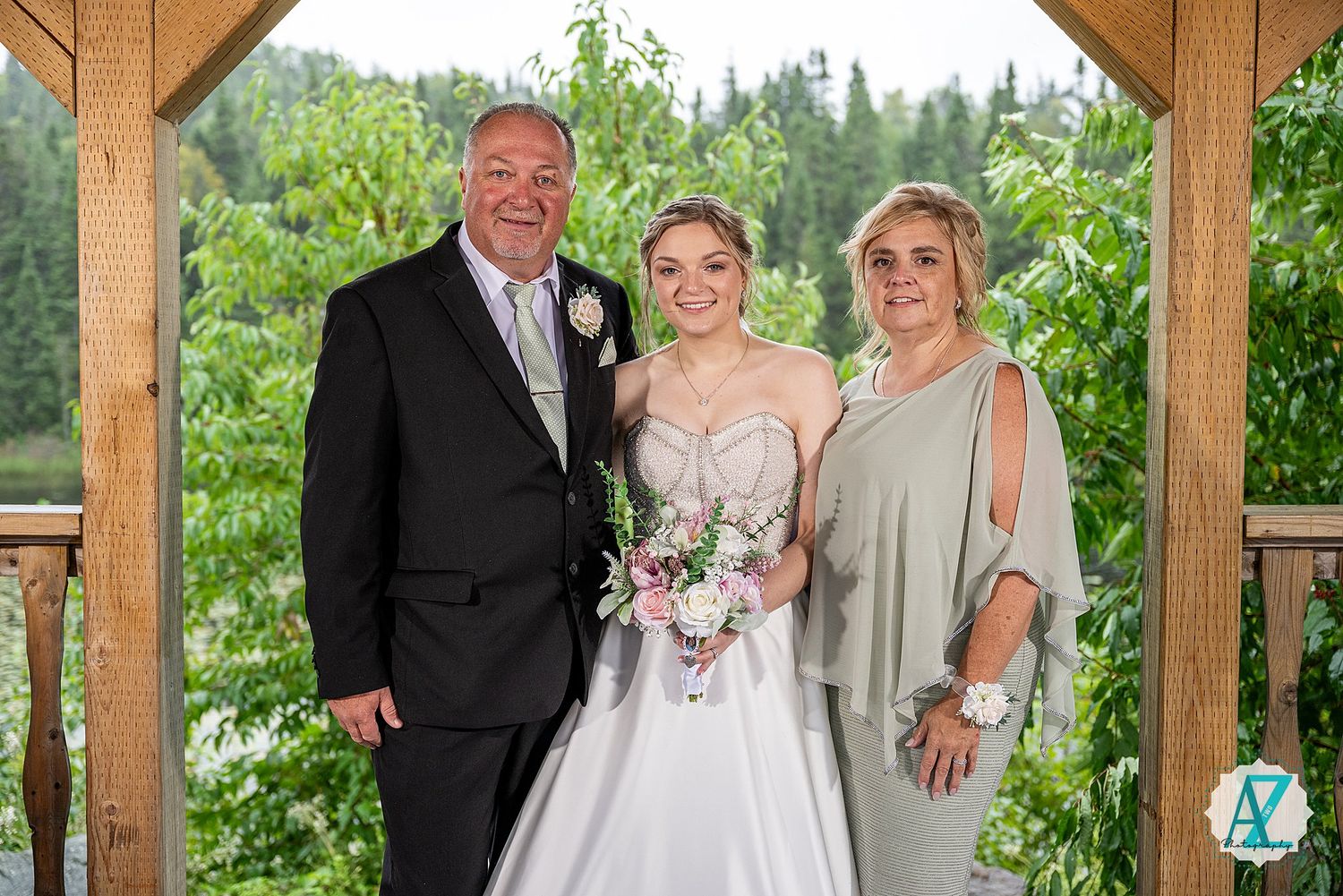 Wedding party celebrates outdoors under rustic wooden pavilion with lush green surroundings.