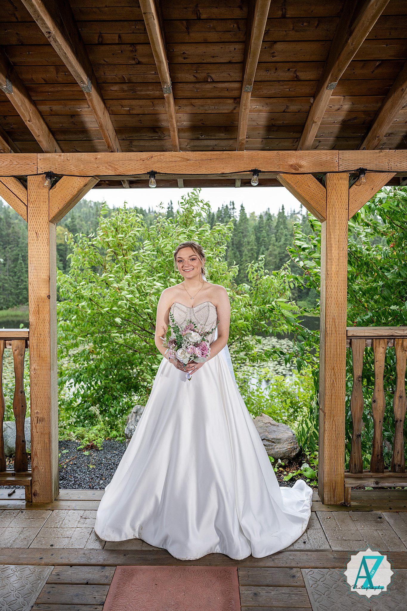 Wedding photo under a rustic wooden gazebo with mountain and forest views in the background.