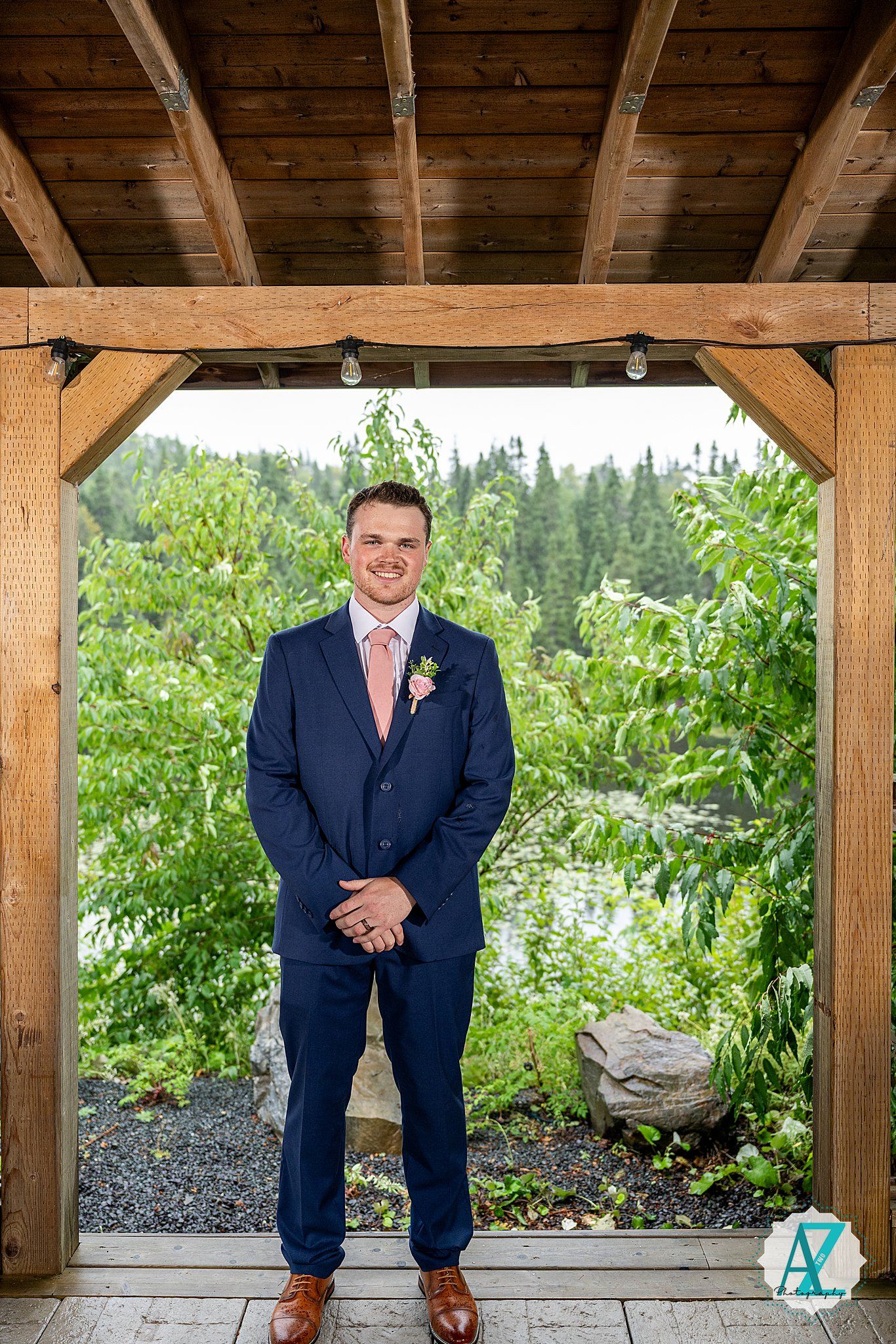 Wedding detail photo showing someone's formal shoes, dress pants and boutonniere against rustic wooden structure.