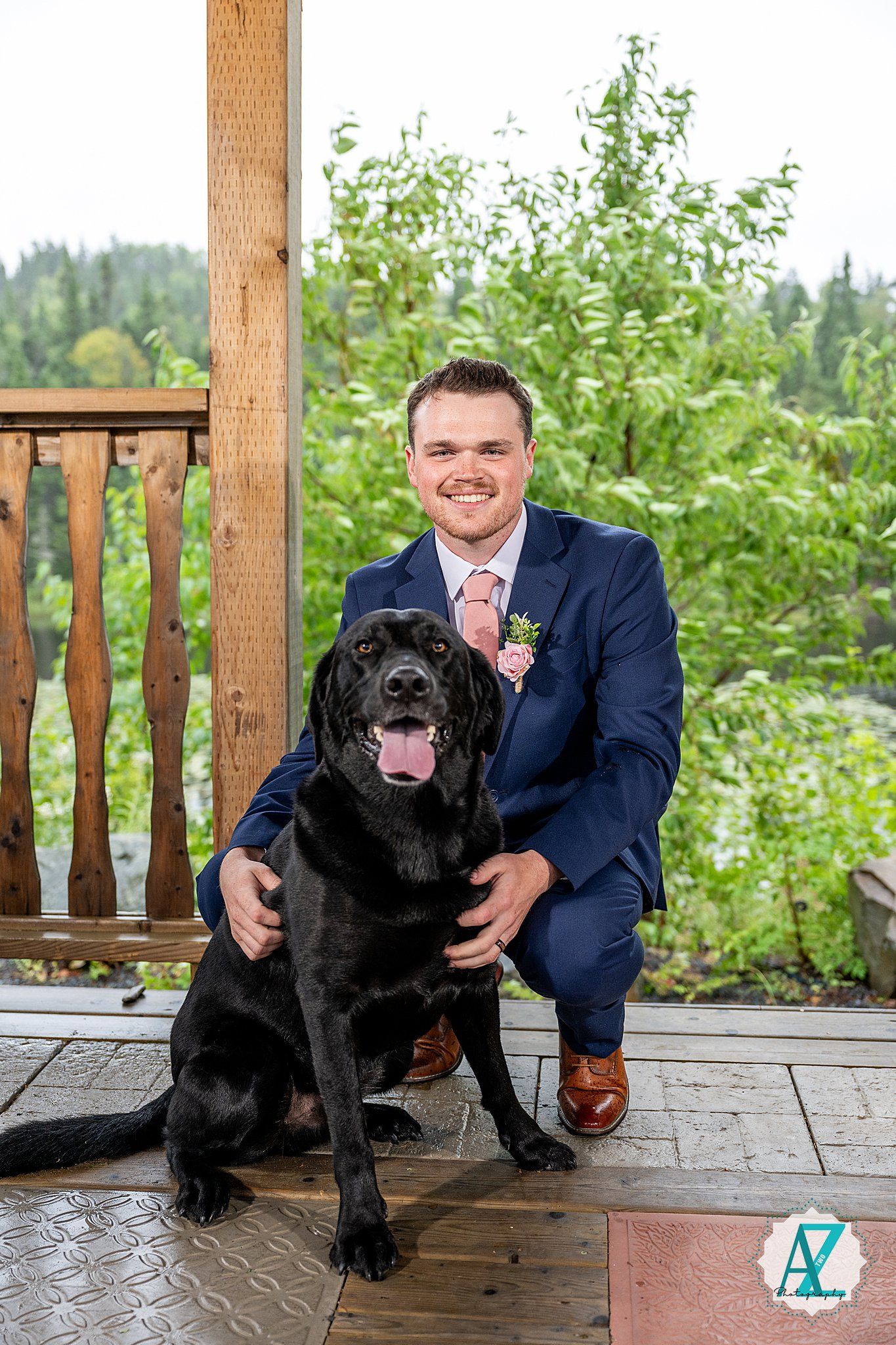 Black Labrador dog poses with owner on wooden deck during wedding celebrations.