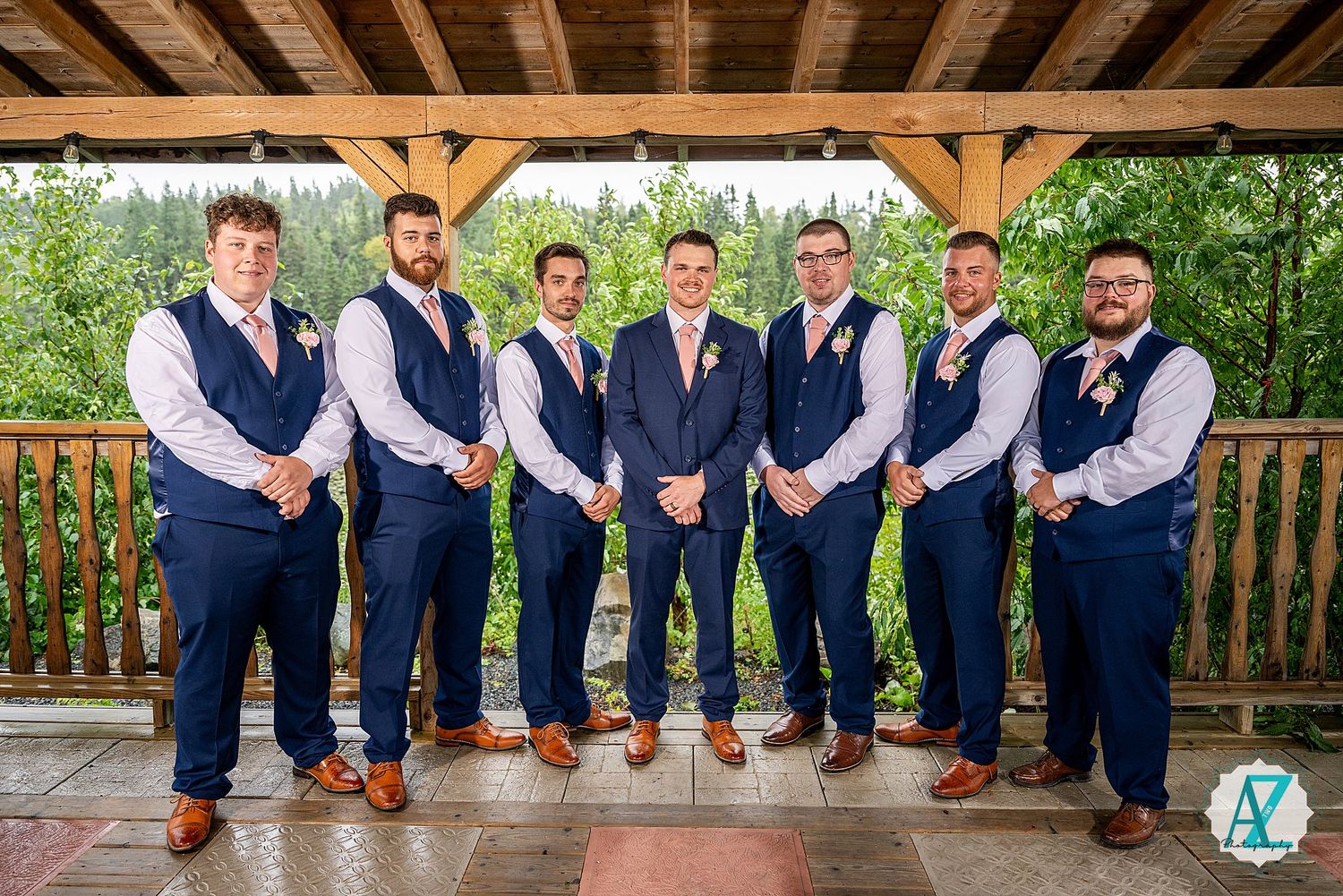 A row of groomsmen in navy suits sit showing their orange socks while posing on a wooden deck ledge.