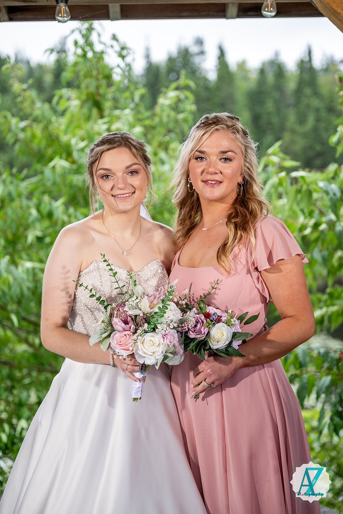 Wedding party members in pink dresses and white gowns pose together while holding floral bouquets outdoors.