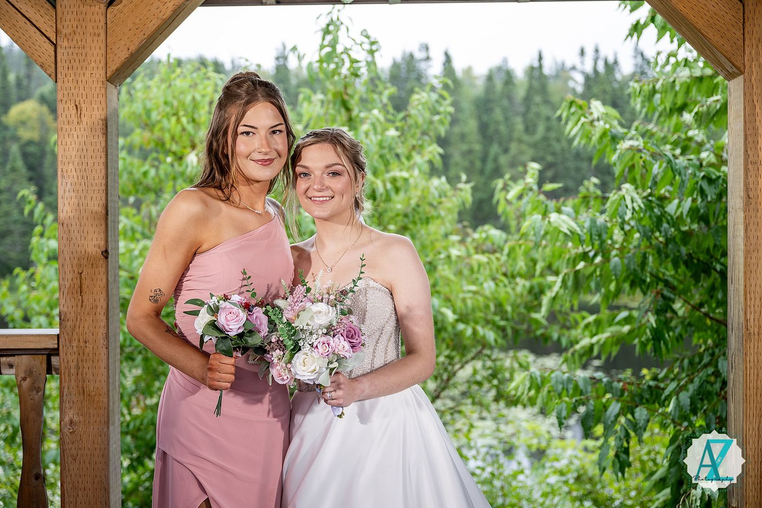 Wedding party in pink and floral dresses gathering under a wooden pergola with natural greenery backdrop.