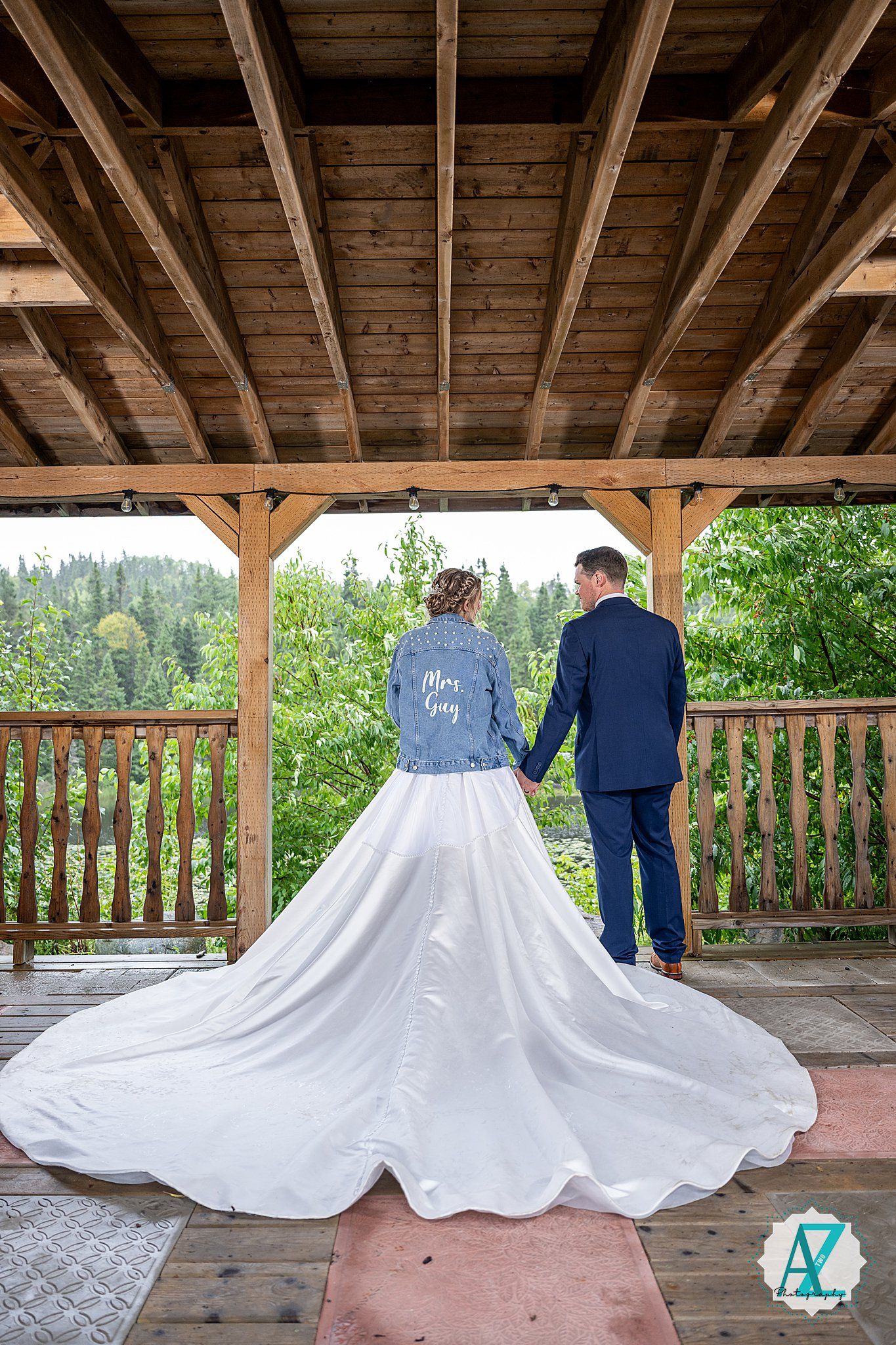 Wedding dresses displayed under wooden pavilion with couples walking in background.